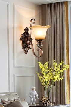 a lamp that is on the wall next to a vase with yellow flowers in it