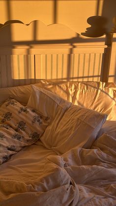 an unmade bed with white sheets and pillows in the morning sun shining on it