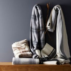 a pile of blankets sitting on top of a wooden shelf next to a gray wall