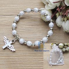 a rosary bracelet with an angel charm on it and a flower bouquet in the background