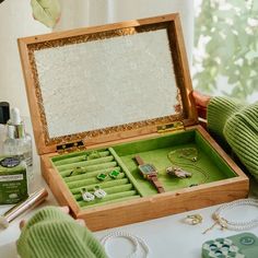 an open wooden jewelry box on a table next to some other items and a person's hand