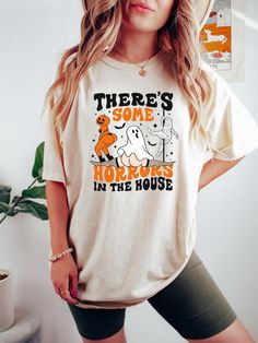 Add some fun and spooky vibes to your Halloween wardrobe with our "There's Some Horrors In The House" apparel featuring a playful twerking ghost design! Perfect for Halloween parties, trick-or-treating, or just getting into the festive spirit, this hilarious and eye-catching design is sure to be a hit. Available in crewneck t-shirt, tank top, and sweatshirt styles, this apparel is the ultimate choice for anyone who loves to bring a bit of humor to the spooky season. Features: -4 Available Colors for T-Shirt: Choose from a selection of Halloween-themed colors that are perfect for making a statement. -2 Available Colors for Sweatshirt: Cozy, comfortable shades that are great for layering on cooler nights. -High Quality Extra Soft Cotton: Enjoy ultimate comfort with our ultra-soft, premium co Halloween Graphic Tee With Funny Print, Halloween Funny Print Graphic T-shirt, Fun Halloween T-shirt Pre-shrunk, Fun Halloween Pre-shrunk T-shirt, Fun Pre-shrunk Halloween T-shirt, Fun Halloween Graphic Print T-shirt, Fun Halloween T-shirt With Screen Print, Halloween Fun T-shirt With Screen Print, Funny Halloween Print Tops