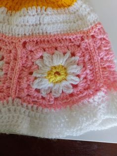 a crocheted hat with a flower on the front and side, sitting on top of a wooden table