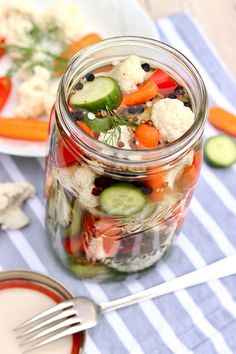 a jar filled with vegetables sitting on top of a blue and white striped table cloth