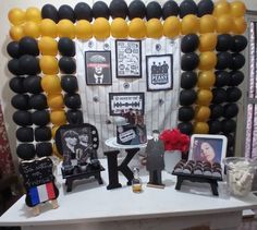 a table topped with black and yellow balloons next to a white table covered in pictures