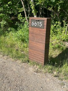 a wooden sign sitting on the side of a dirt road next to a lush green forest