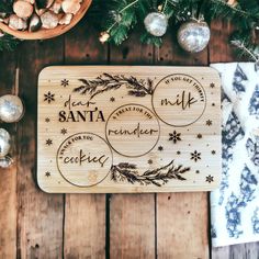 a wooden cutting board with the words santa and reindeer on it next to christmas decorations