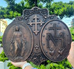 a person holding up two metal plaques in front of some bushes and trees with crosses on them