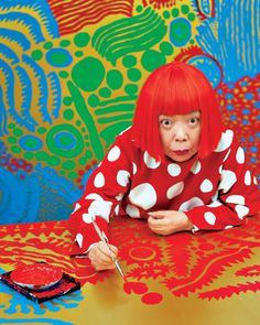 a woman with red hair sitting at a table in front of a colorful wallpaper