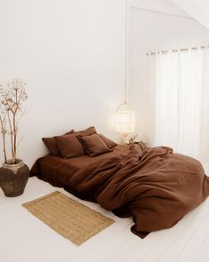 a bed sitting on top of a white floor covered in brown sheets and pillows next to a potted plant