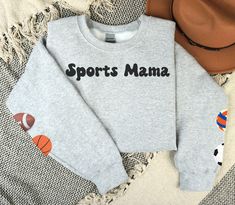 Sports Mama Sweatshirt, Sport Ball Sleeve Sweatshirt, Custom Basketball, Custom Football, Custom Volleyball, Custom Tennis, Custom Soccer, Custom Baseball Mom Shirt These are the perfect sweatshirts for sports moms of all kinds.  You can place the balls on the sleeves that represent the sports your children play. The Gildan sweatshirts are very comfy, and you will want to wear them all season long while curling up with your favorite book and hot beverage.   B R A N D S  We do partner with several providers and use multiple brands of clothing and other products in our shop. We source American and responsibly made products whenever possible.  The following are the current brands we use for our clothing designs: Bella + Canvas  Comfort Colors® Deco (Slides) Gerber Childrenswear Gildan Rabbit Team-colored Sweatshirt For Sports, Team-colored Sports Sweatshirt, Varsity Sweats With Ribbed Cuffs For Sports, Sporty Sweatshirt For Sports Season, Athletic Heather Sportswear Sweatshirt For Sports Season, Athletic Heather Sweatshirt With Ribbed Cuffs For Sports, Collegiate Moisture-wicking Sweatshirt For Sports, Sporty Sweatshirt For Sports, Team Spirit Sweatshirt With Team Name For Sports