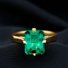 an emerald colored ring sitting on top of a black cloth