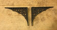 two black metal brackets on a wooden surface with holes in the middle and one is shaped like an arrow