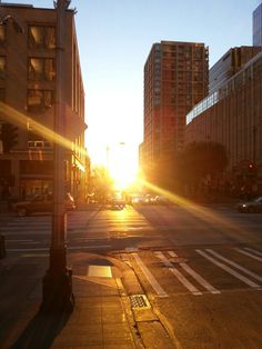 the sun is setting on an empty city street with tall buildings in the back ground