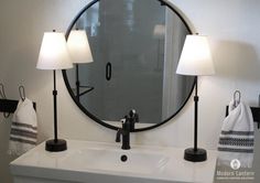 a bathroom sink with two lamps and a round mirror