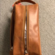 a brown leather bag with zippers on the inside is laying on the floor in front of a carpeted area