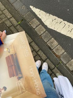 a person holding a book on the street with their legs crossed and one hand in front of them