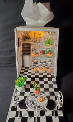 a dollhouse kitchen with black and white checkerboard flooring, potted plants in the middle