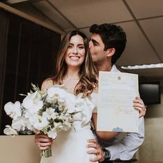 a bride and groom pose for a photo holding their wedding paper in front of them