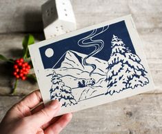 a hand holding up a card with an image of mountains and pine trees on it