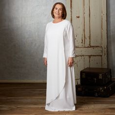 a woman standing in front of an old door wearing a long white dress and matching shoes