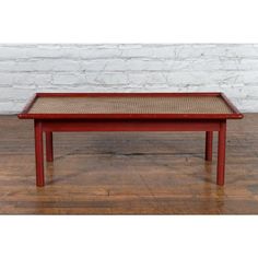 a red coffee table with wicker top on wooden floor next to white brick wall