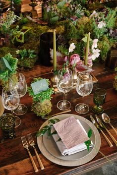 a wooden table topped with plates and glasses filled with flowers, candles and napkins