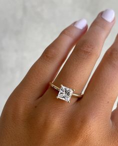 a woman's hand with a diamond ring on top of her finger and white nails