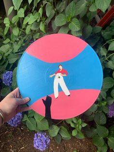 a hand holding a frisbee with a person on it in front of purple flowers