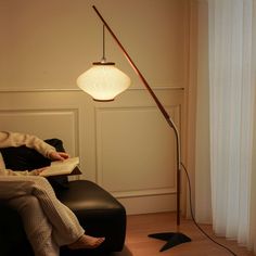 a woman sitting on a couch reading a book under a lamp in a living room