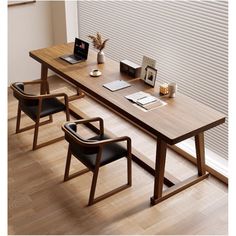 a wooden table with two chairs and a laptop on it, in front of a window