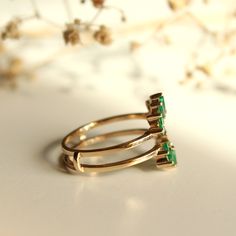 three gold rings with green stones sitting on top of a white table next to flowers