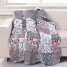 a quilted blanket with flowers on it sitting on top of a white couch next to a window