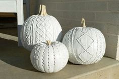 three white pumpkins sitting on the ground next to a brick wall and cement block