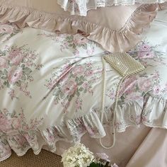 a bed with pink and white flowers on the comforter next to a flower vase