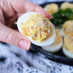 a person holding an egg in their hand with other food on the plate behind them