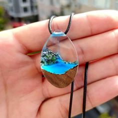 a hand holding a glass pendant with a landscape in it