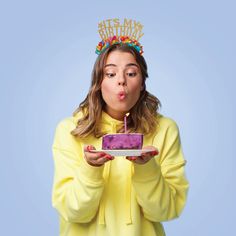 a woman in a yellow shirt blowing out a candle on a cake that is sitting on a plate