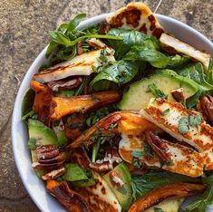 a white bowl filled with lots of food on top of a stone counter next to a knife