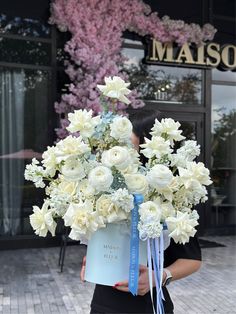 a woman holding a bouquet of white flowers in front of a storefront with the name maiso on it