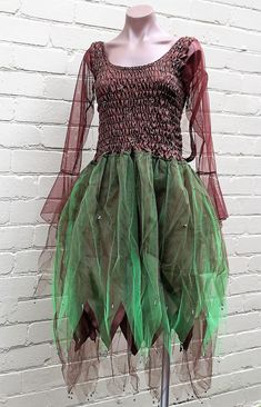 a mannequin wearing a green and red dress on a display stand in front of a white brick wall