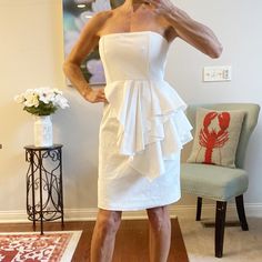 a woman standing in front of a mirror wearing a white dress and holding her hand up to her face