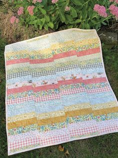 a quilt is laying on the ground in front of some pink and yellow flowers,