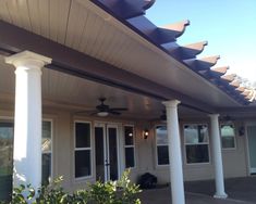 an outdoor covered patio with ceiling fans and white columns on the side of the house