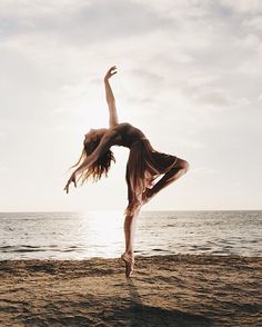 a woman is doing a handstand on the beach by the ocean with her legs in the air