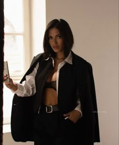 a woman in a black suit and white shirt holding a cell phone up to her chest