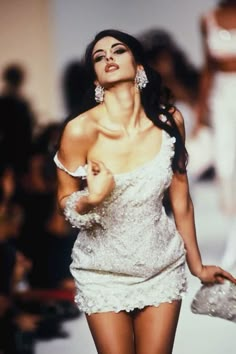 a woman is walking down the runway in a short white dress and holding a purse