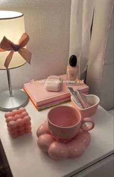 a table topped with pink items next to a lamp and a cup filled with liquid