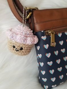 a crocheted cupcake keychain hanging from a purse on a white furnishing