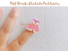 a hand is holding a small piece of beaded fabric with a pink heart on it